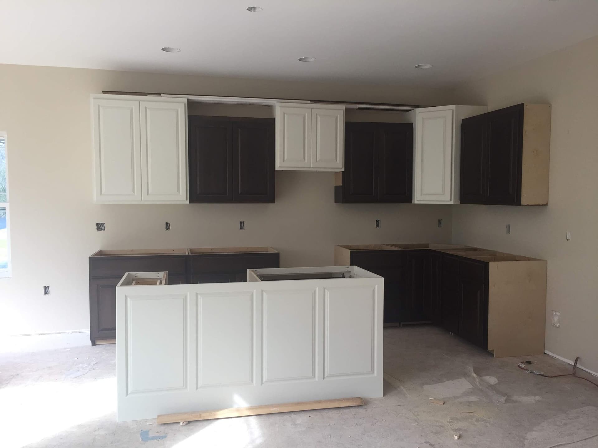 Kitchen with white upper cabinets and near-black lowers, with the white island set in place before countertops.