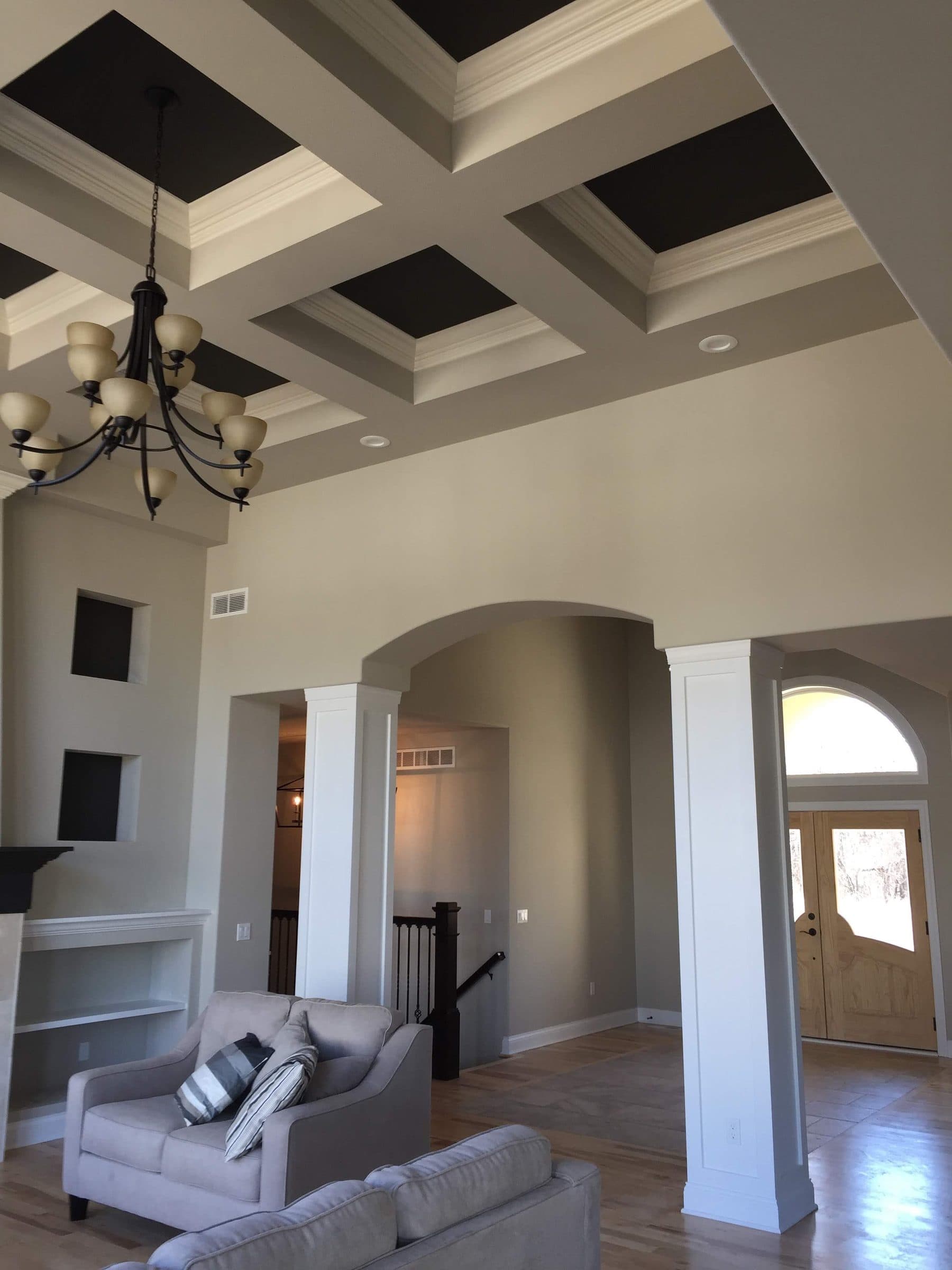 The black coffered ceiling seen from the entry, with white columns and an archway framing the great room below.