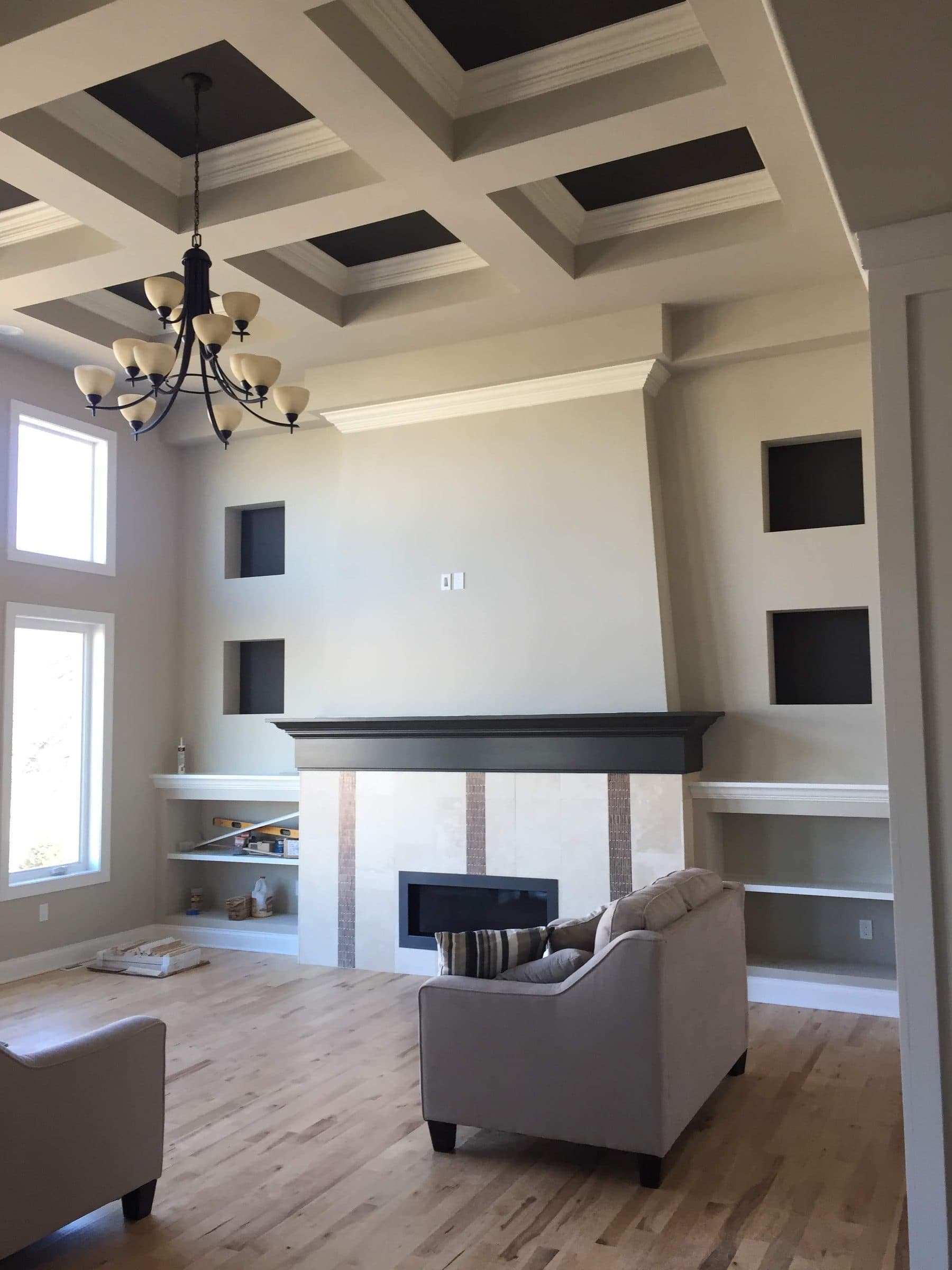 Two-story great room with a black coffered ceiling above a full-height fireplace and built-in display niches.