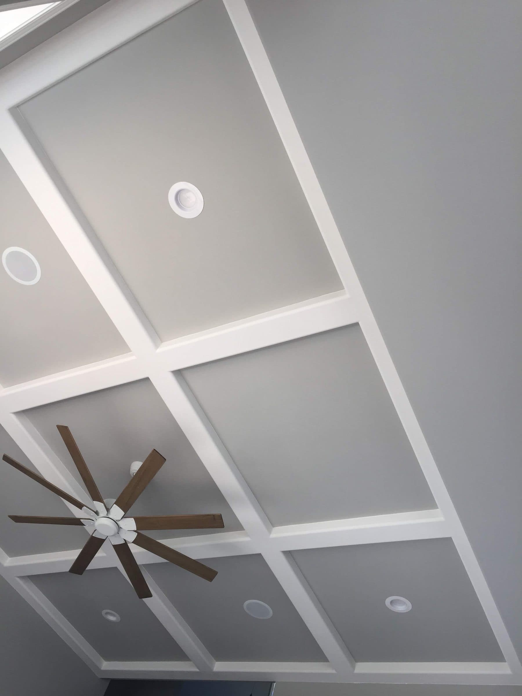 Gray coffered ceiling panels inside white beams, with recessed lights and a ceiling fan.