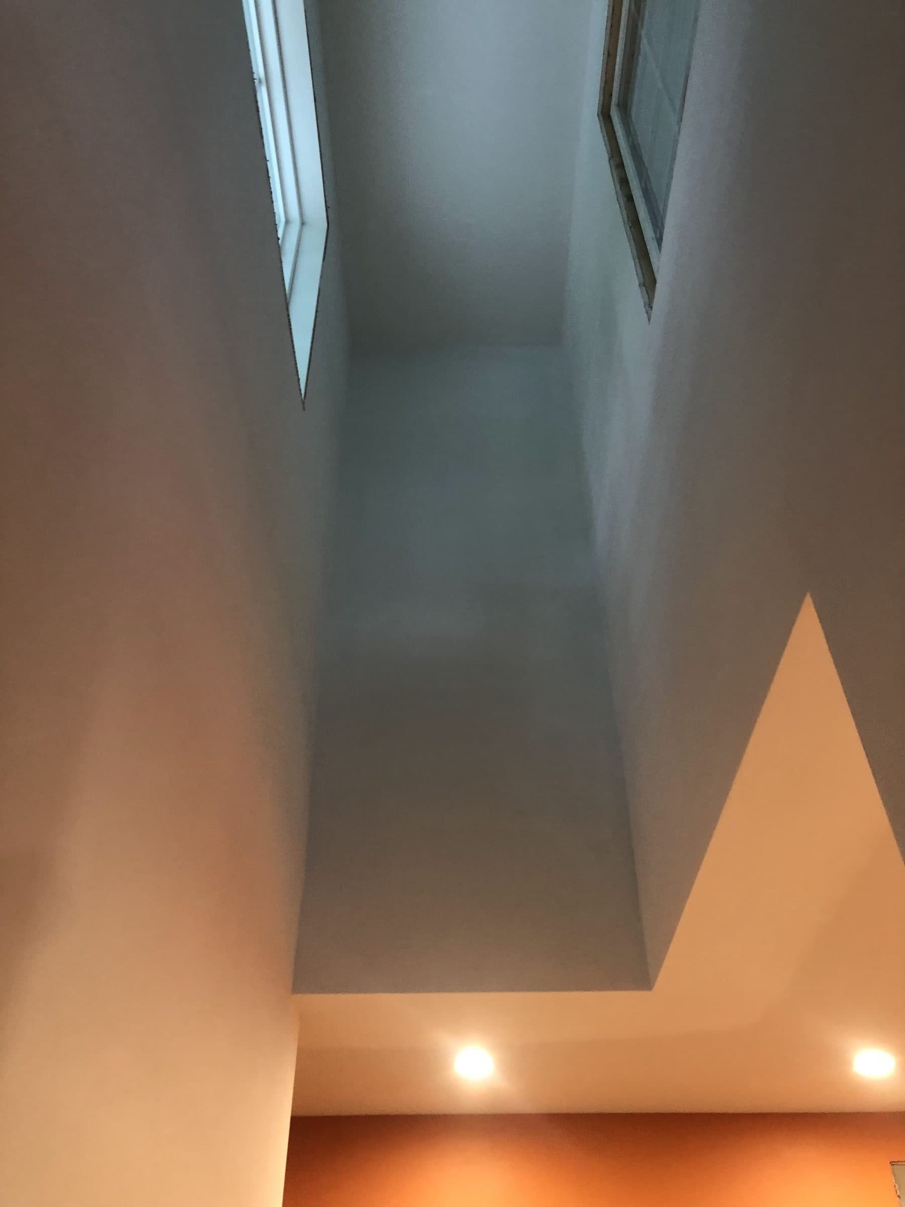 Two-story stairwell ceiling and walls cut in and rolled from staging, with a skylight at the top.