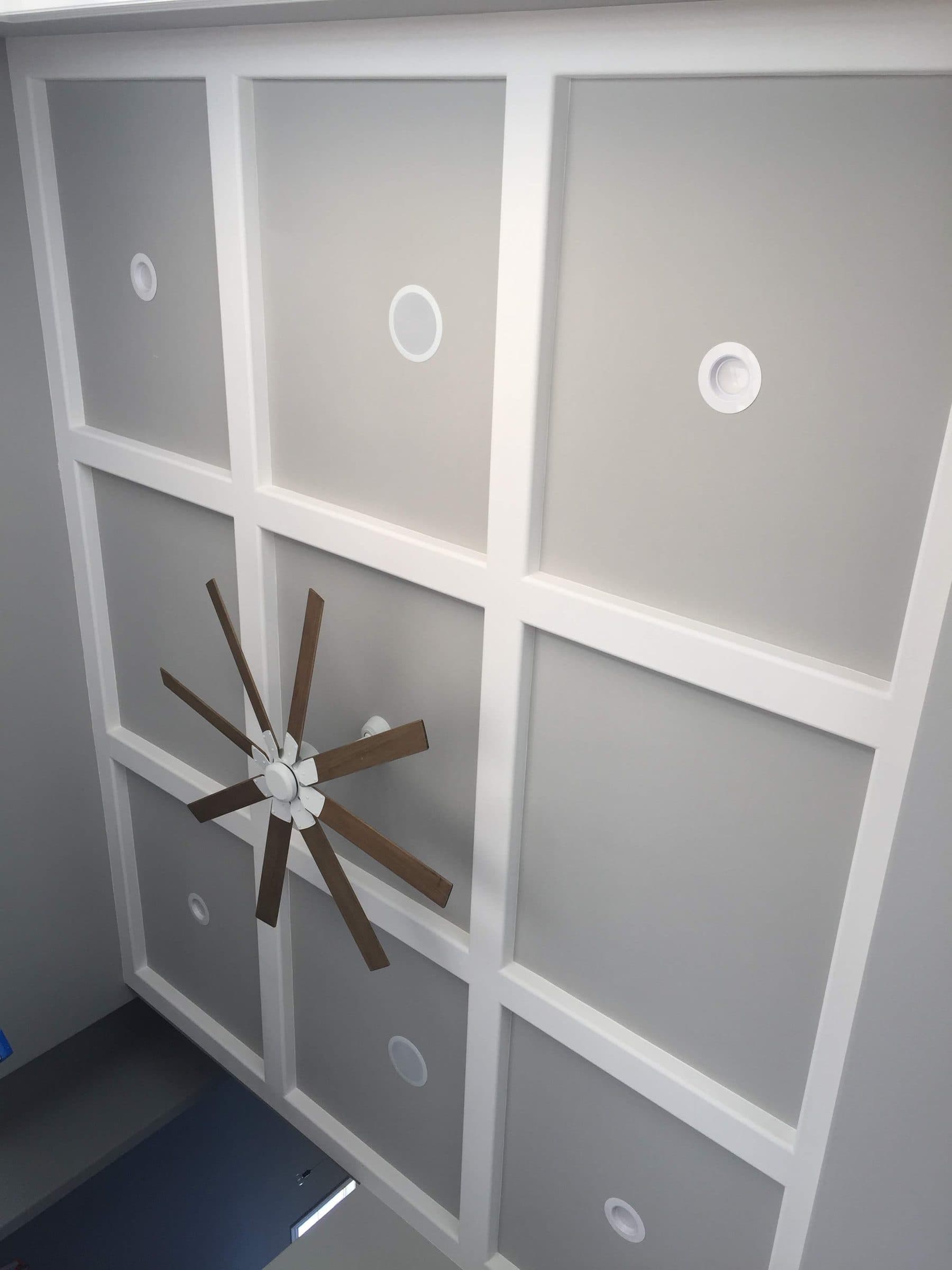 Grid-patterned coffered ceiling in two tones of white and gray with a wood-bladed fan at its center.