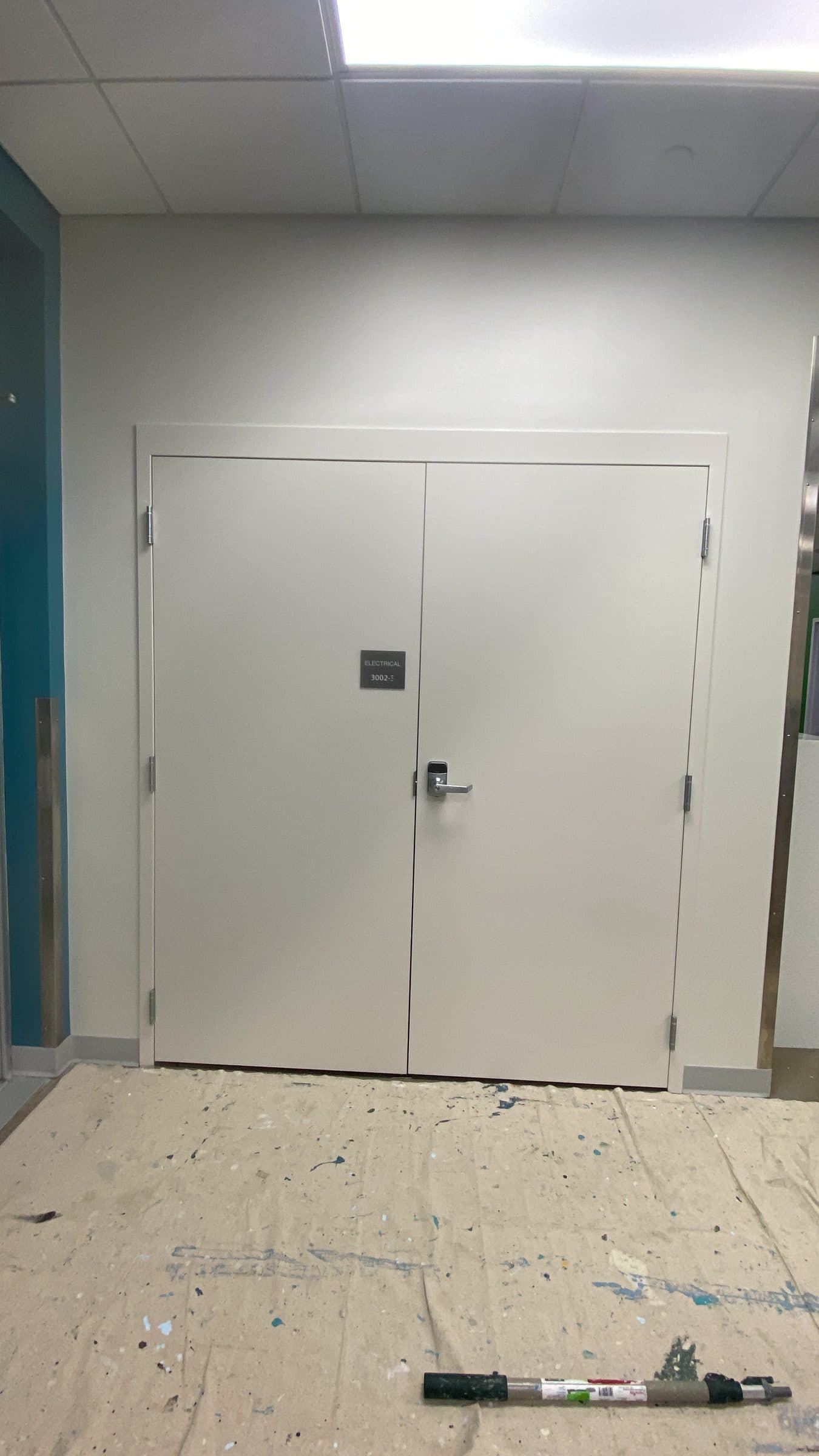 A pair of hollow metal corridor doors and frame recoated in off-white, with the floor still protected below.