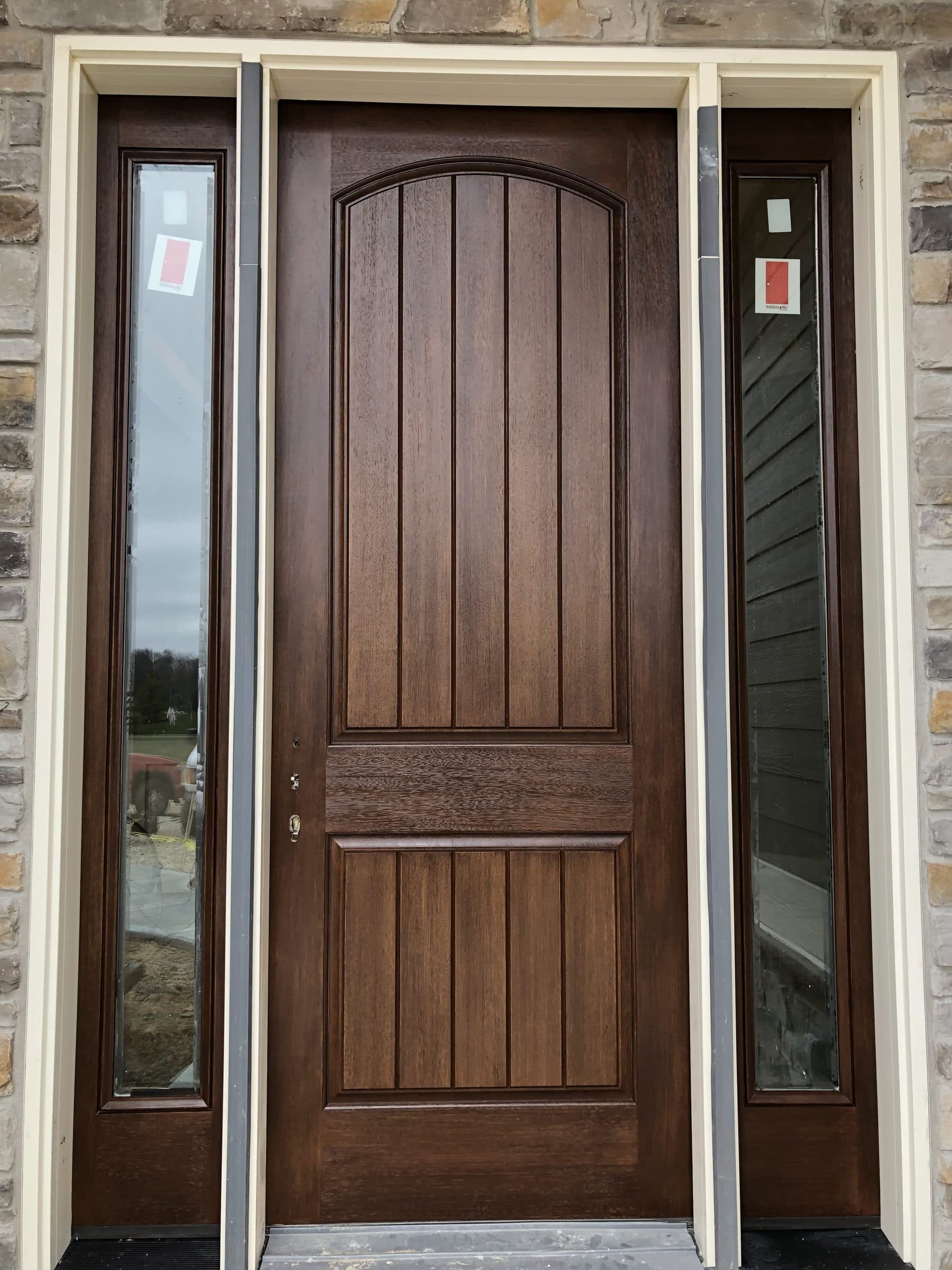 Square-on view of a brown-stained plank entry door and its two full-height sidelights, showing the stain matched evenly across all three.