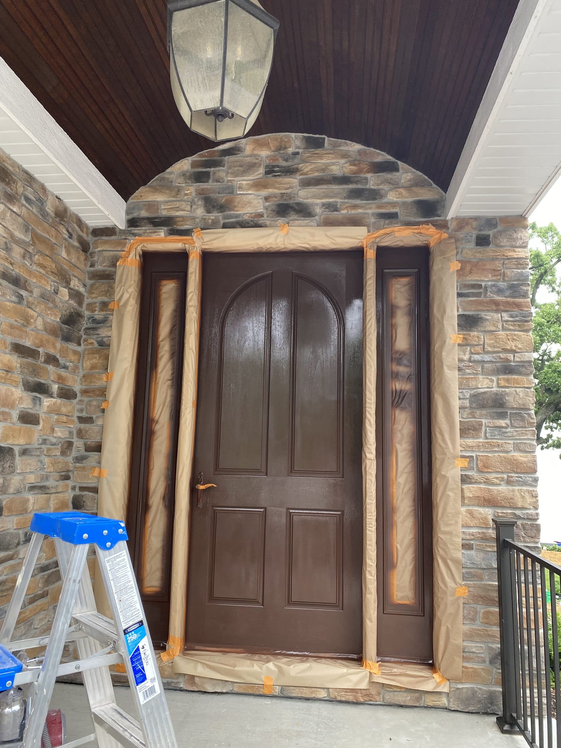 The same arched entry part-way through the job, with the sidelights and stone surround masked off in paper and a step ladder in the porch.