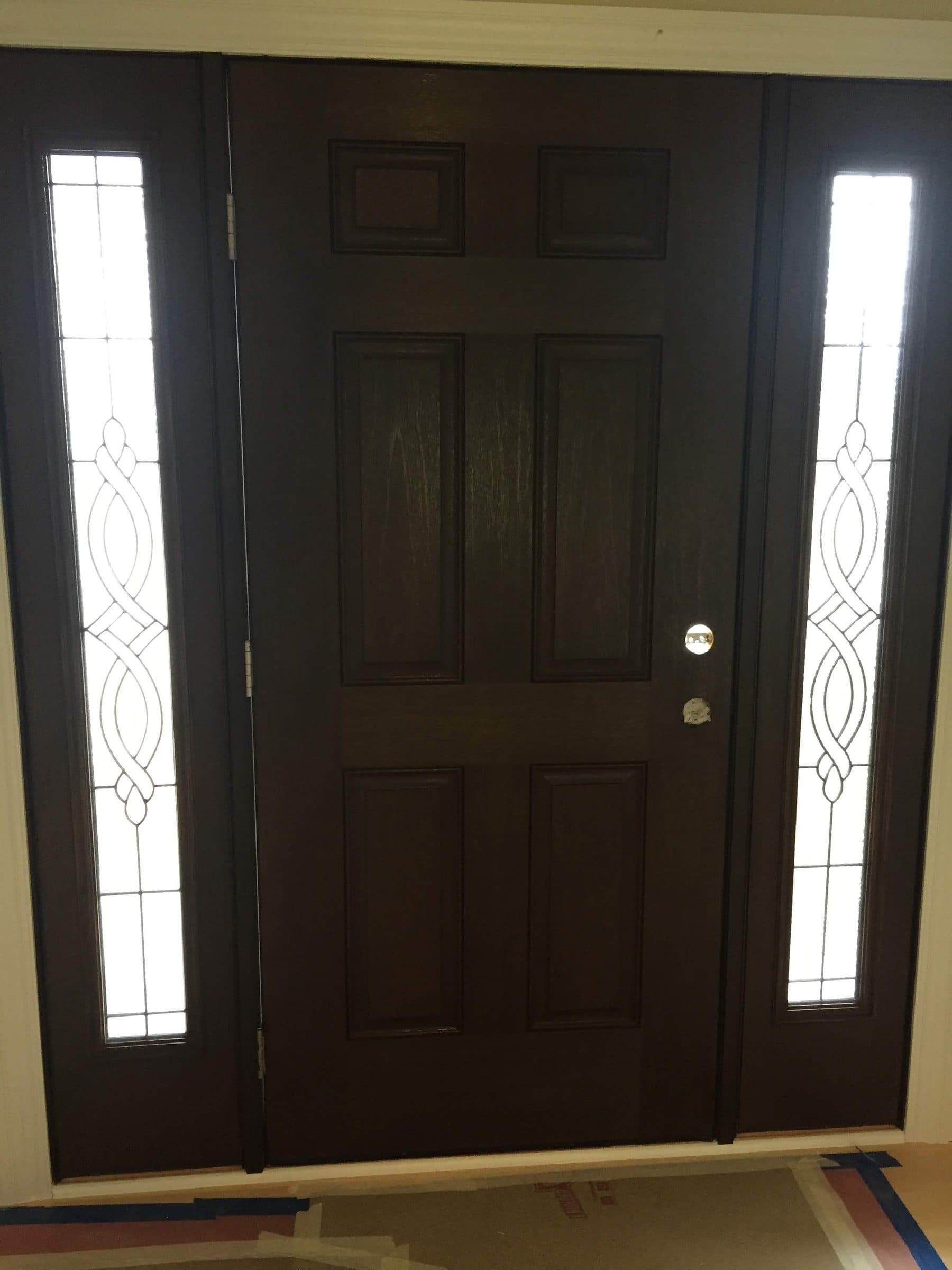 Near-black stained six-panel entry door flanked by two leaded glass sidelights with a beveled oval pattern.