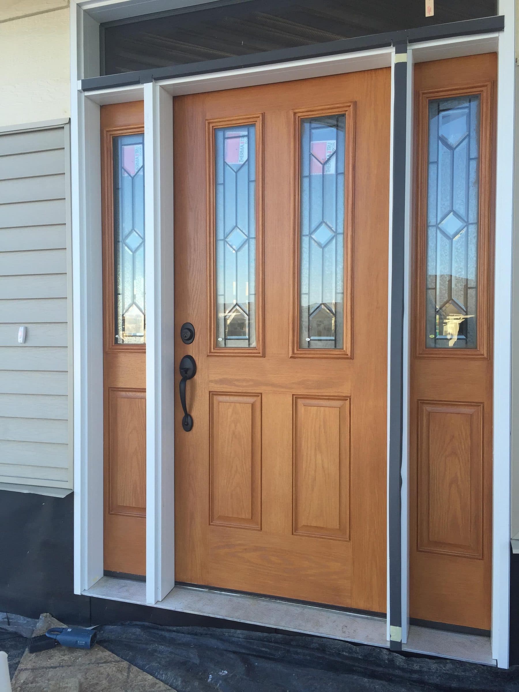 Light oak-stained entry door with three beveled leaded glass panels and matching sidelights, set in white casing.