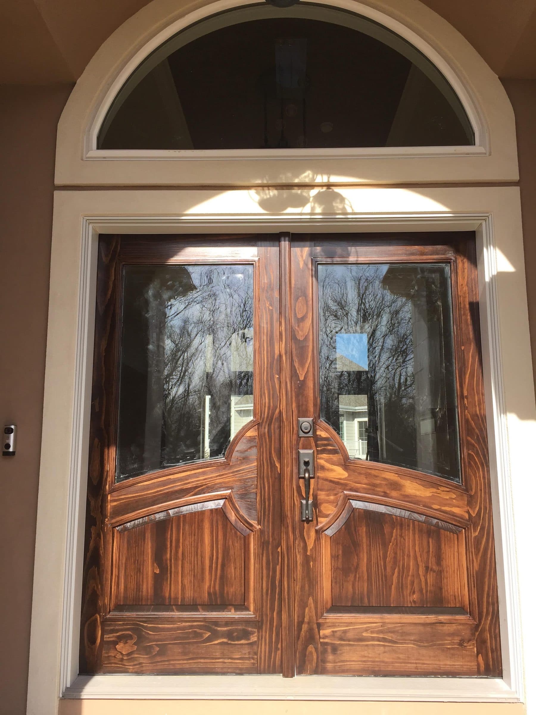 Stained pine double entry door with a matching arched transom above, the grain reading strongly through the finish.