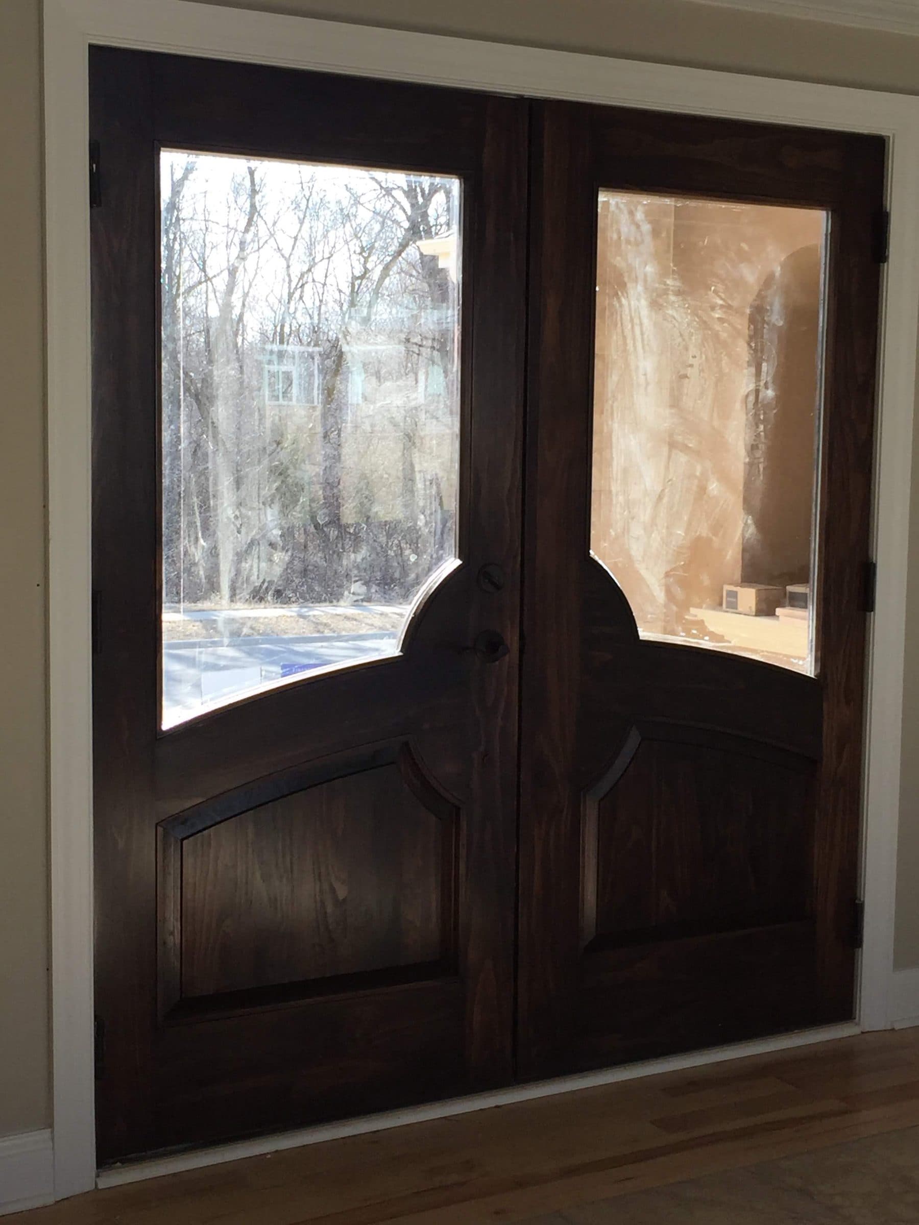 Stained pine double entry door with tall arched glass panels, photographed from inside the entry.