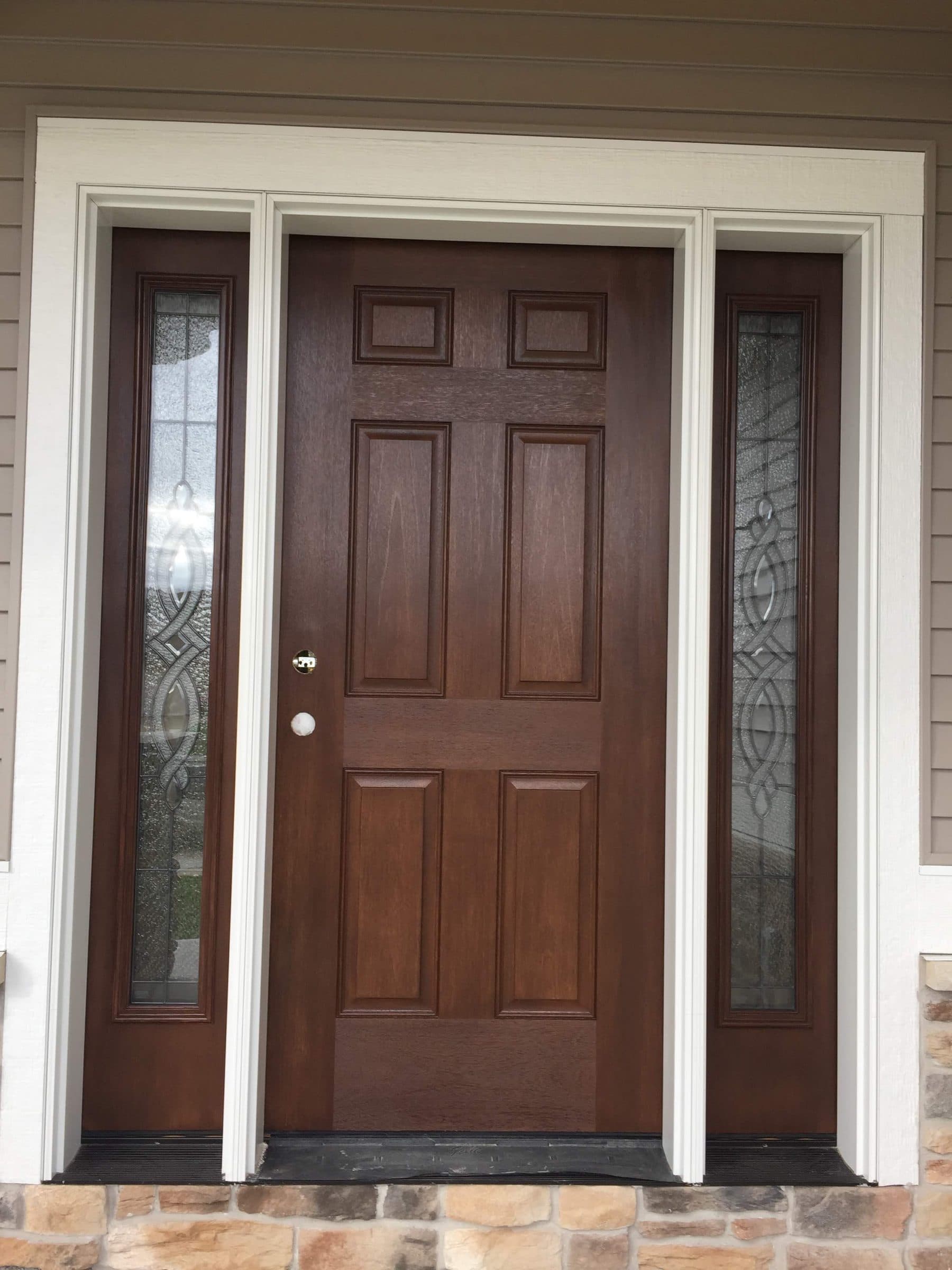 Brown-stained six-panel entry door flanked by two beveled leaded glass sidelights in white casing above a stone step.