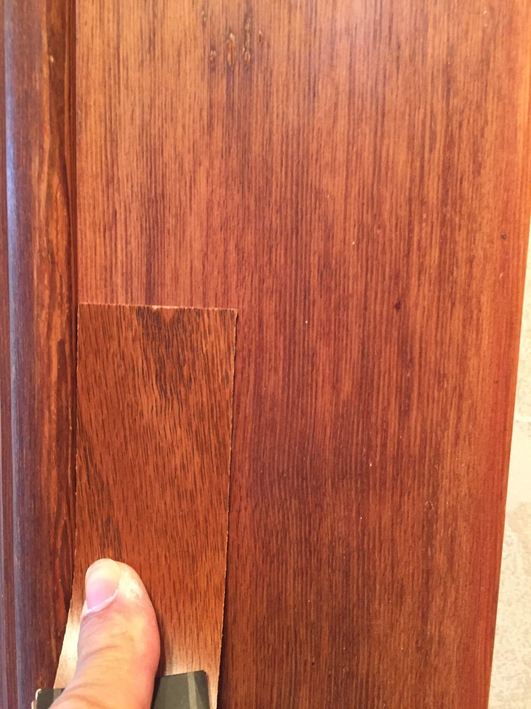 A hand holding two stain sample boards against an existing door to match the color before any finish is applied.