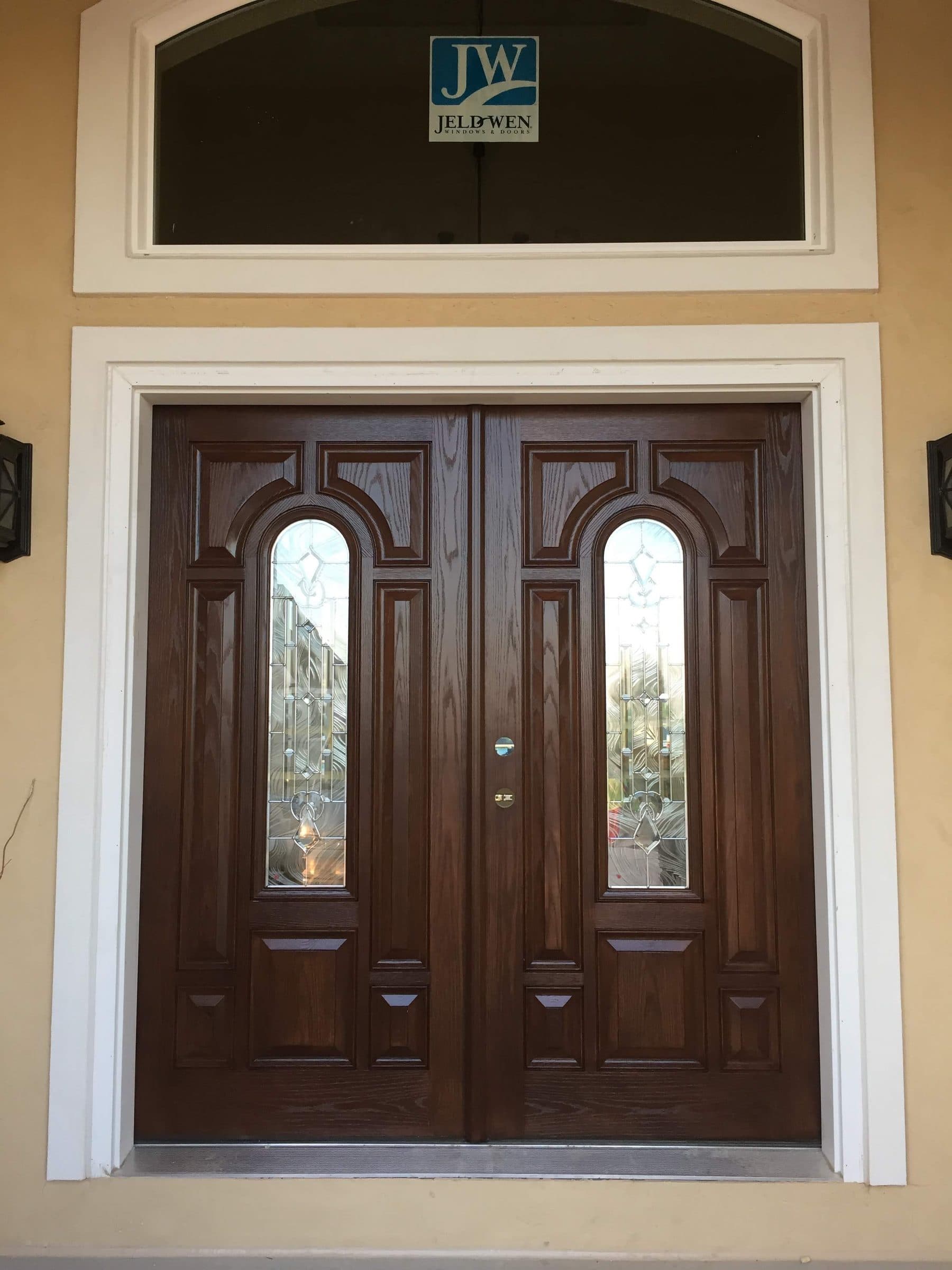 Stained double entry door with two arched glass panels and an arched transom above, freshly finished on a new build.