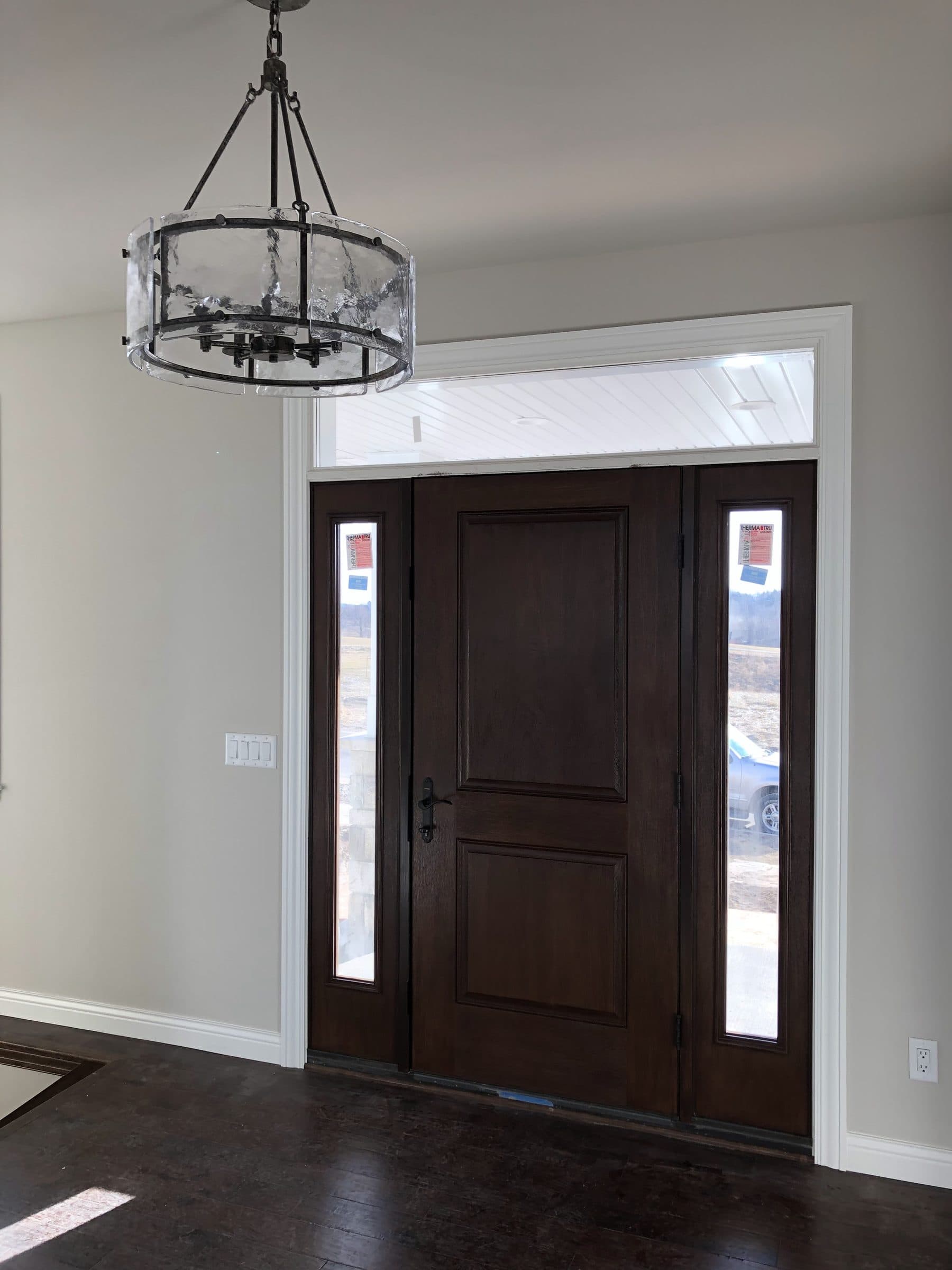 Stained fiberglass entry door and sidelights seen across a foyer under a black lantern chandelier.