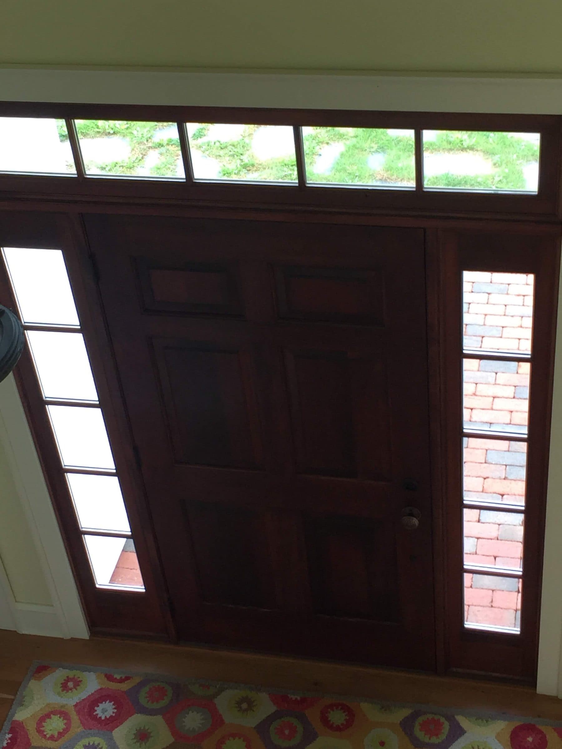 Dark-stained entry door photographed from the foyer, with a four-pane transom above and sidelights looking out onto brick.