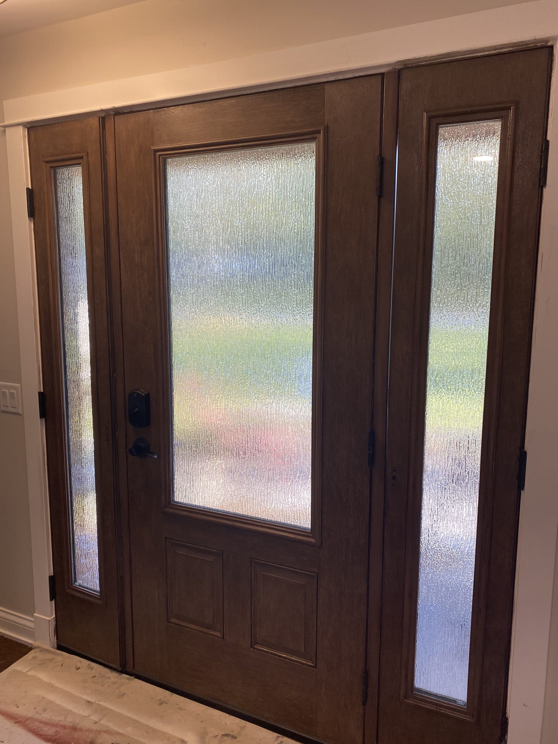 Brown-stained entry door with a large frosted glass panel and two matching frosted sidelights, seen from the entry hall.