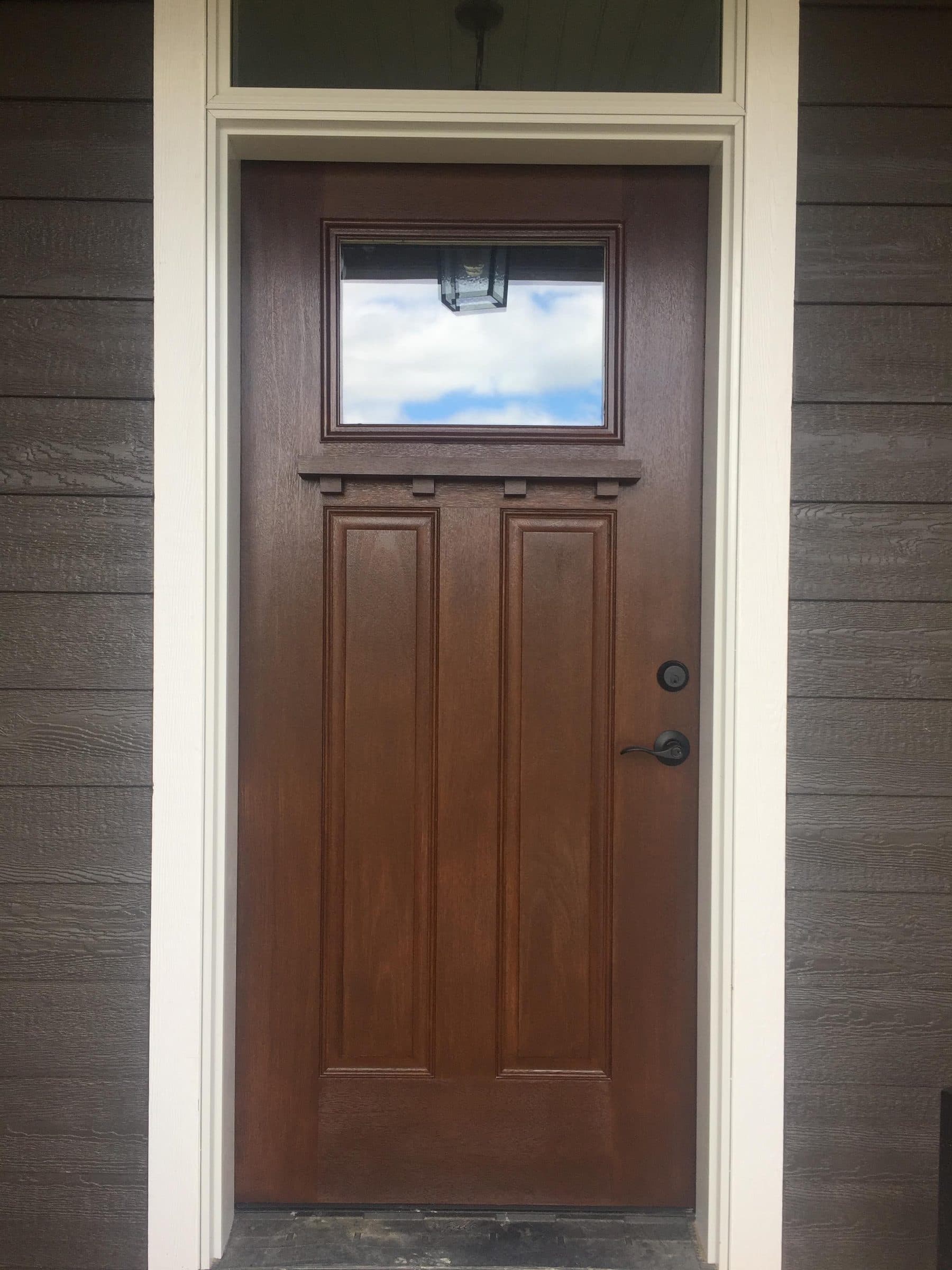 Square-on view of the stained entry door and its transom, showing the grain running evenly through both.