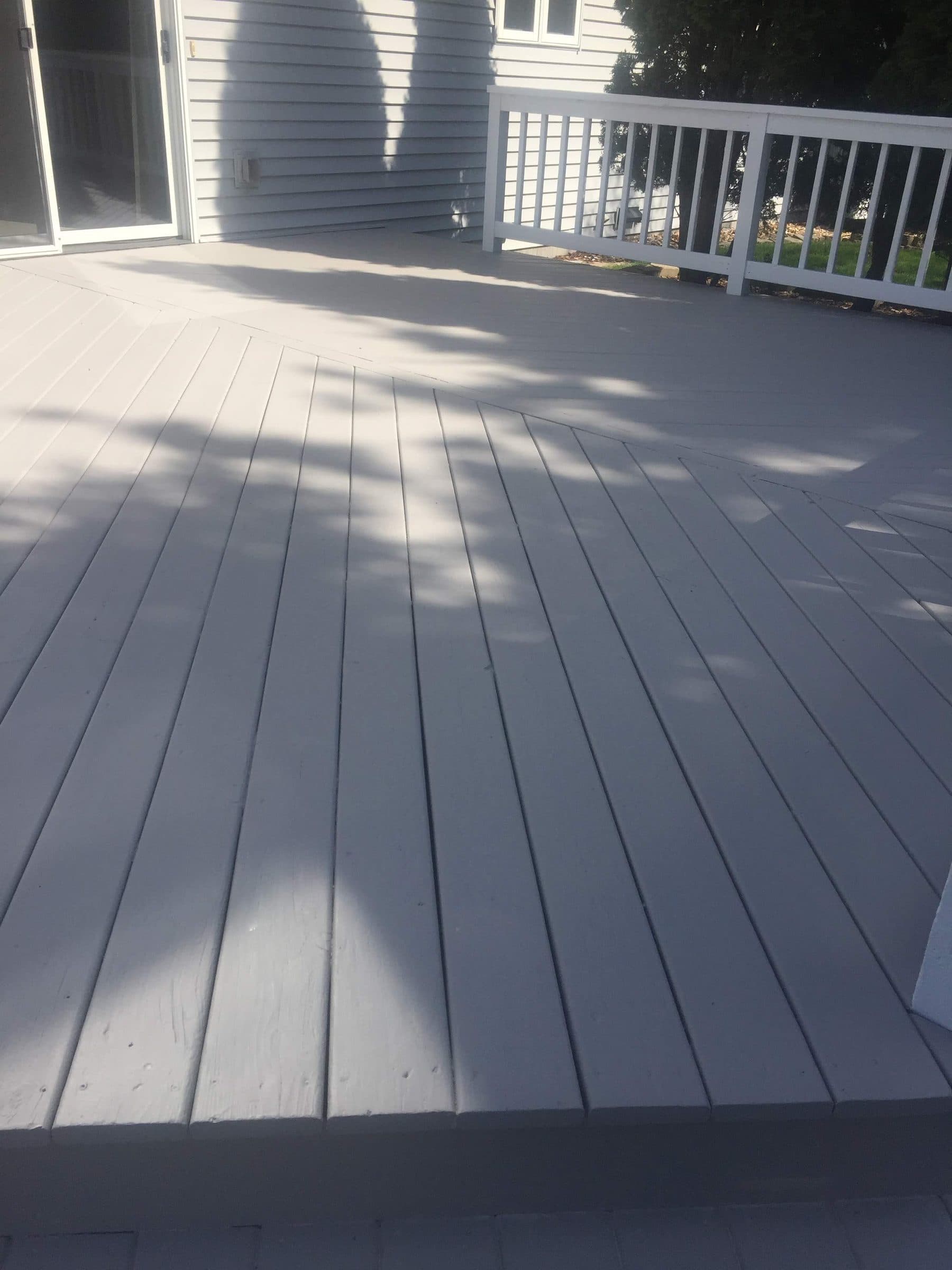 Gray-stained deck boards running to a white rail, the coating even across every board end.