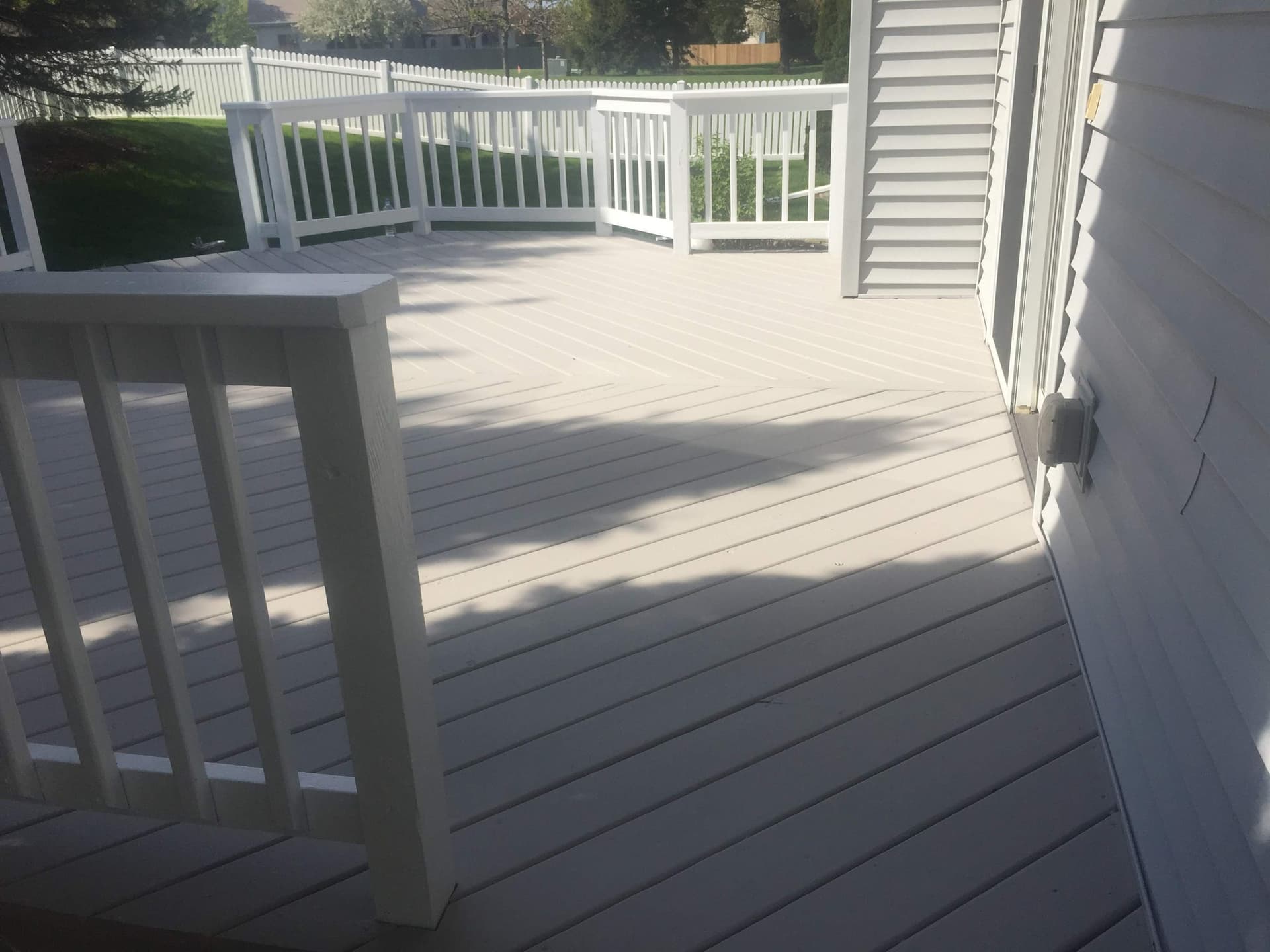 White painted deck rail and post detail against the gray stained decking and white siding behind.