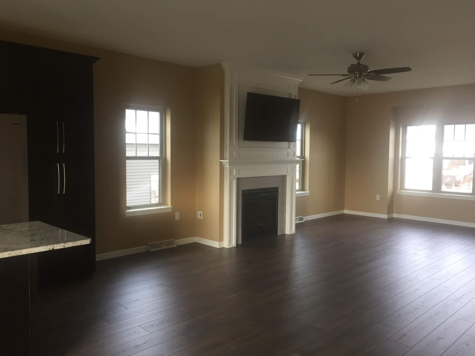 Finished great room with a white fireplace surround, a dark accent wall and dark hardwood floors, cleaned up and handed back.