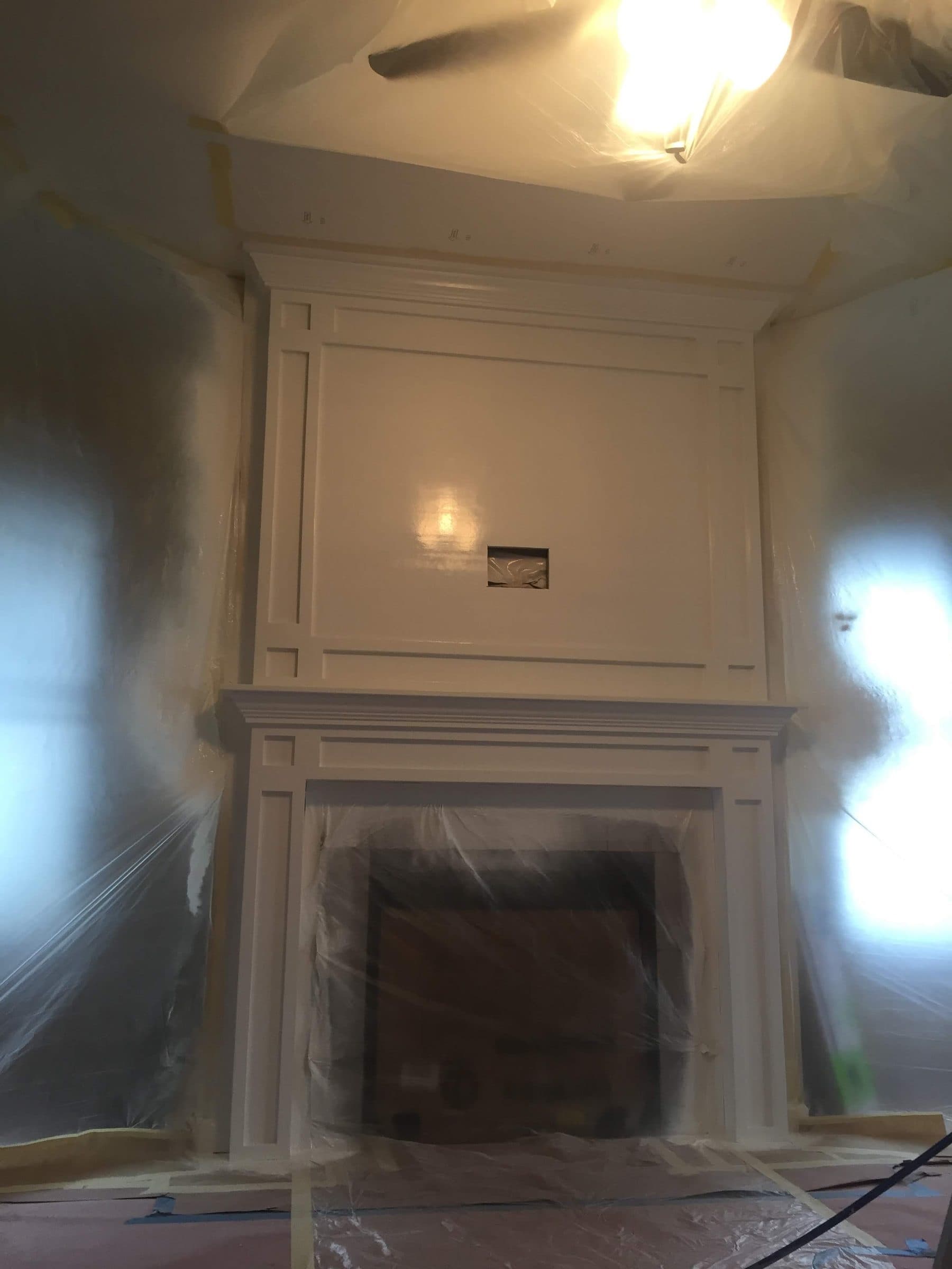 Fireplace surround and mantle sheeted in plastic and taped off before spraying, with the floor fully covered.