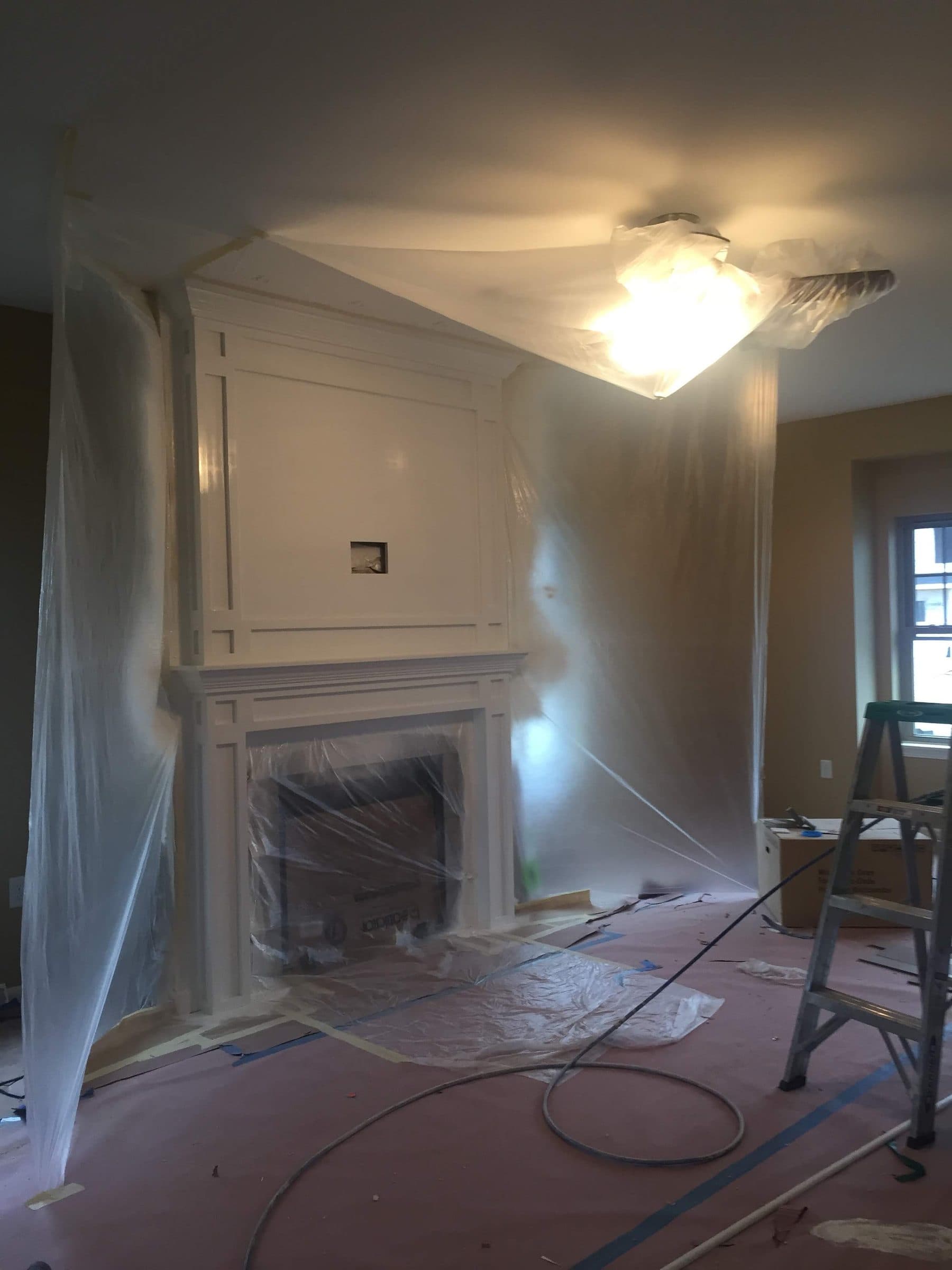 Wider view of the same room fully masked for spraying, with plastic run to the ceiling, floors covered and the sprayer hose laid in.