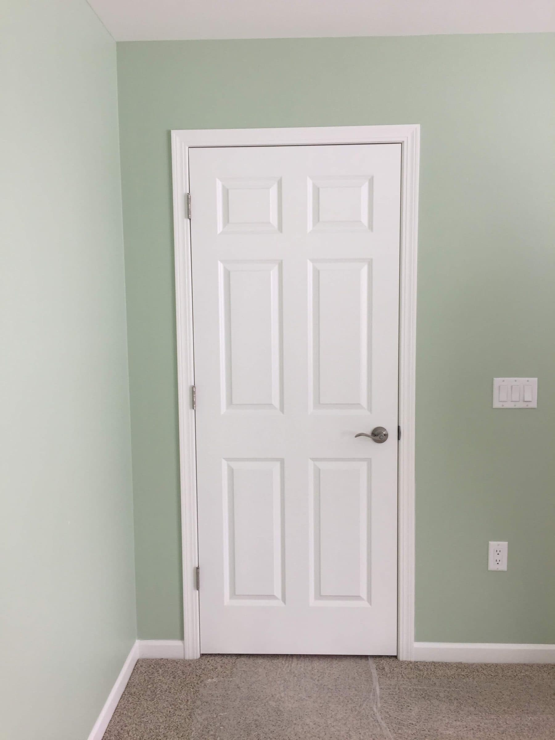 Sage green wall meeting a white six-panel door and casing, with the cut line held straight the full height.