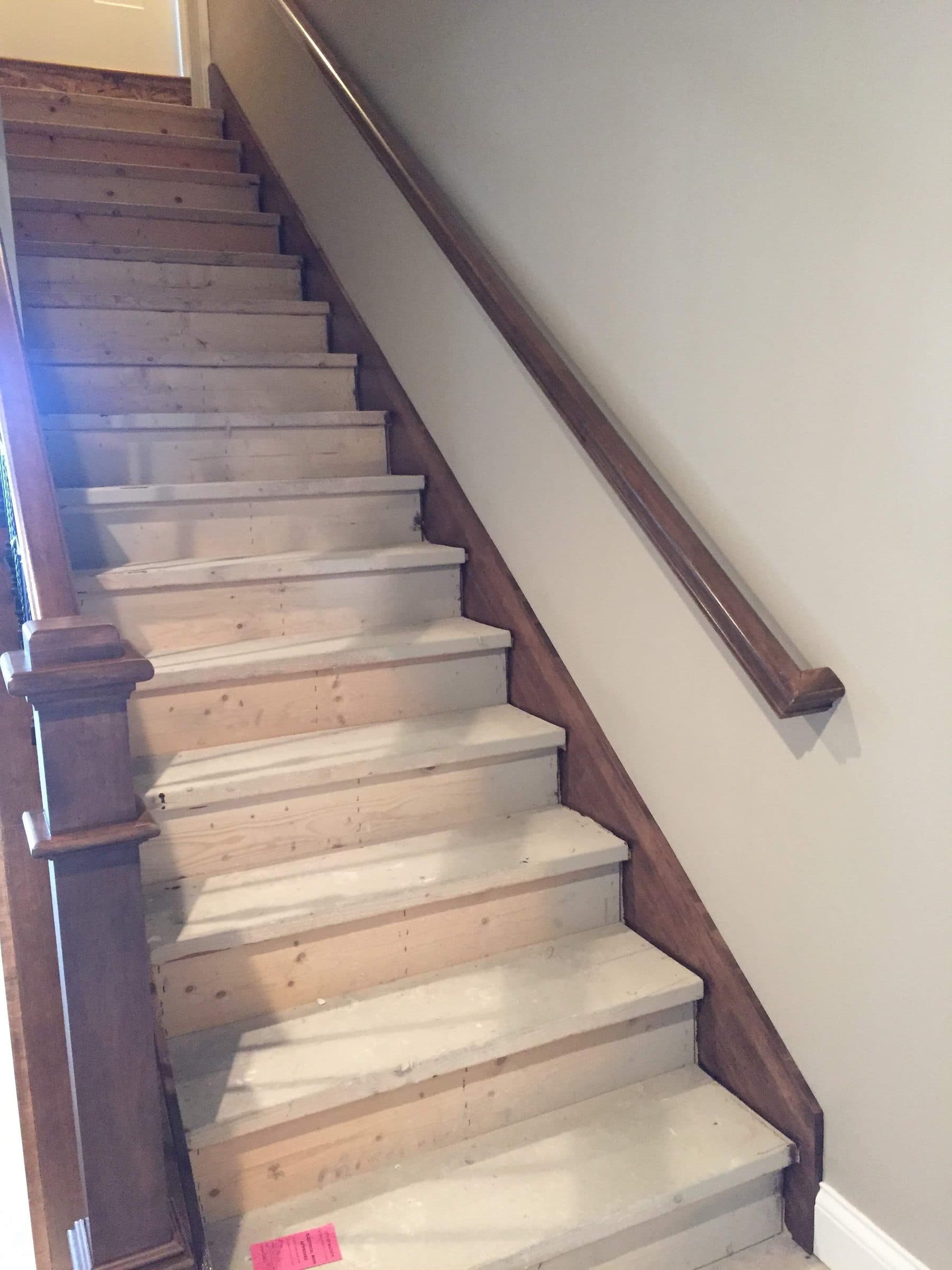 Stained wall-mounted handrail running down a basement staircase beside freshly painted gray walls.