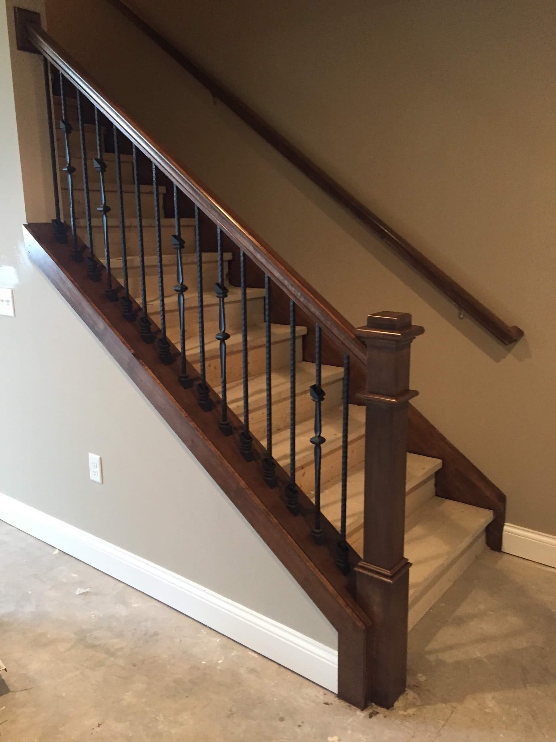 Stained handrail, newel post and black iron balusters on a staircase above bare stair treads.