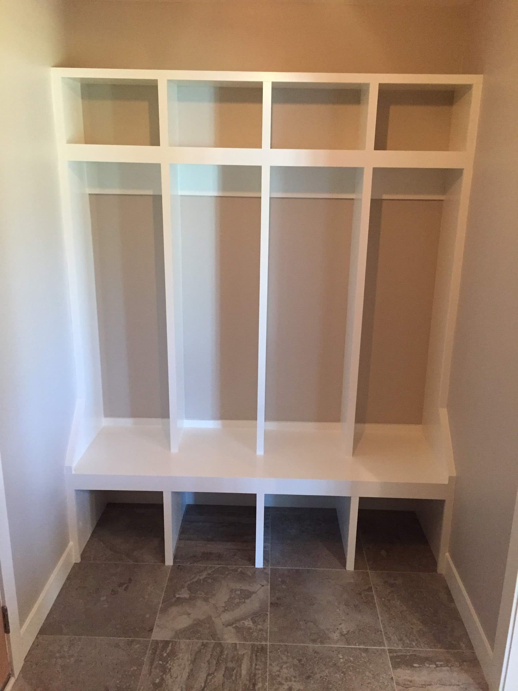 Mudroom built-in with bench, cubbies and hanging space, sprayed white above tile flooring.