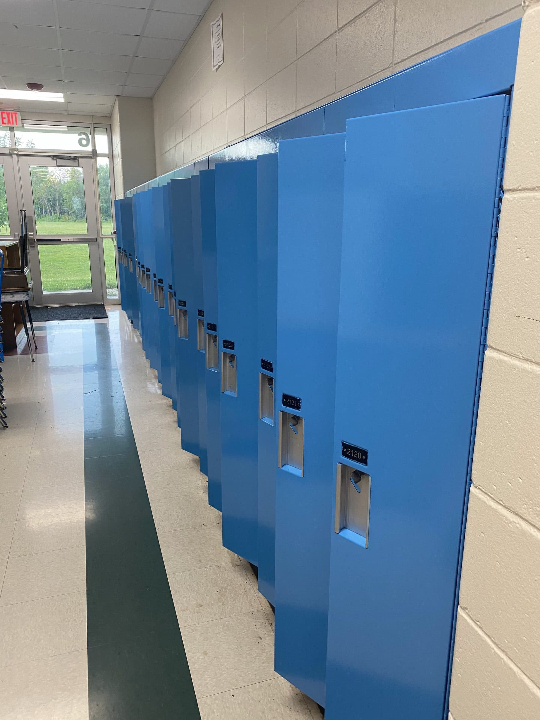 A run of school lockers refinished in two blues along a block corridor with a green terrazzo floor.