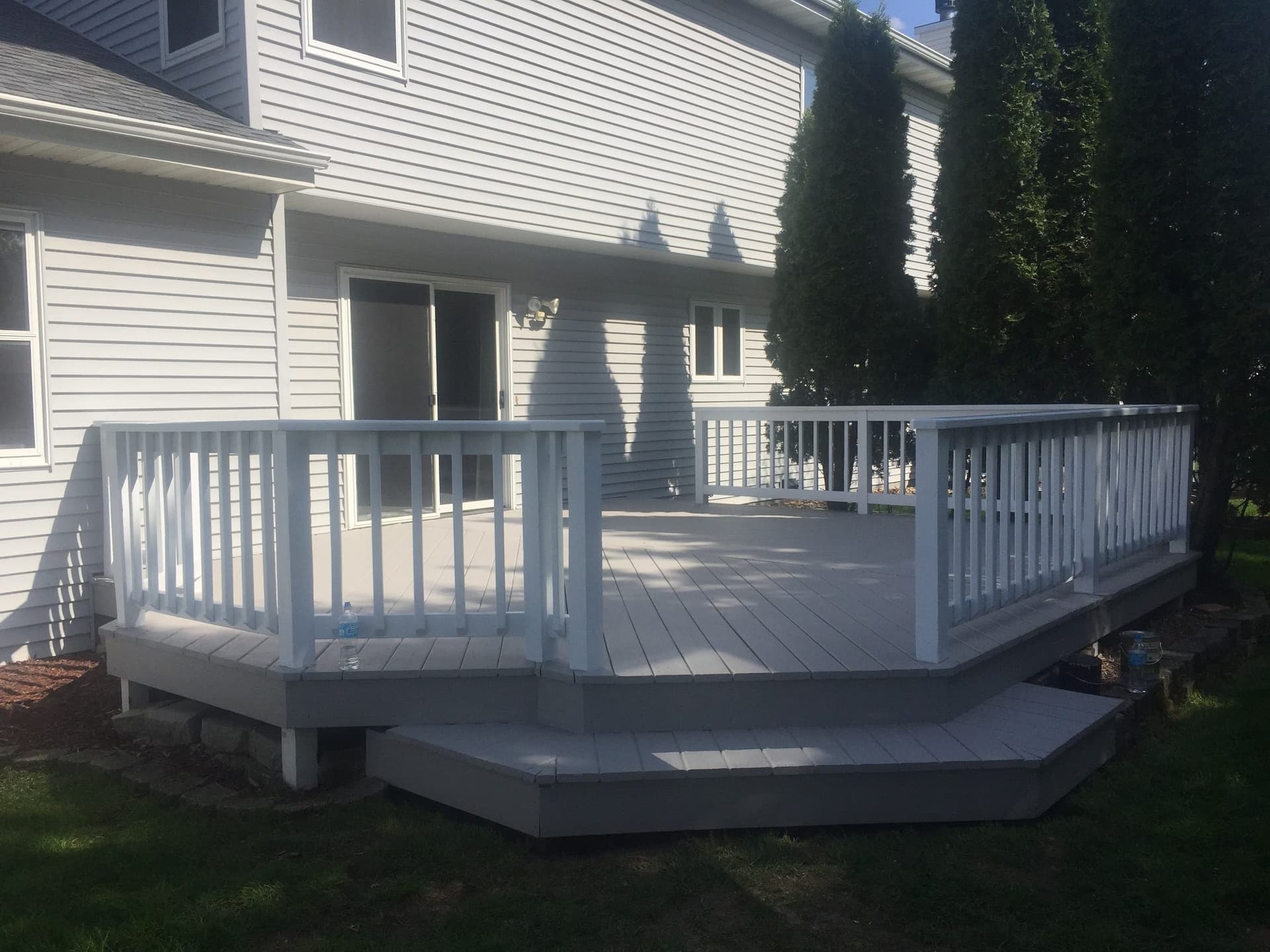 Gray-stained deck with a white painted rail and skirt, wrapping the corner of a white sided house.